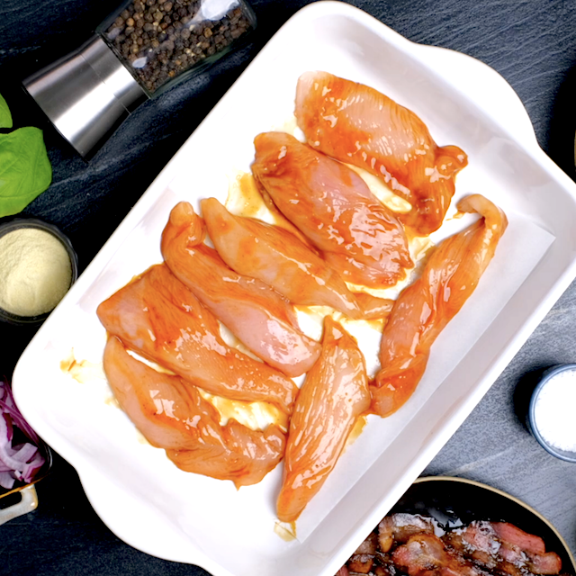 Chicken tenderloin fillets coated with BBQ sauce in a baking dish.