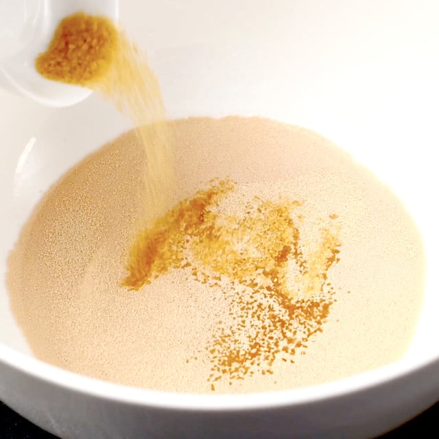 Brown sugar being added to yeast mixture in a bowl to make BBQ chicken pizza dough.