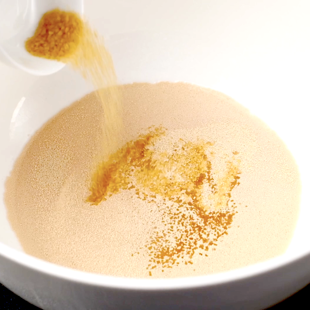 Brown sugar being added to yeast mixture in a bowl to make BBQ chicken pizza dough.