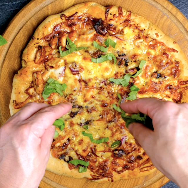 Chopped basil being sprinkled over freshly baked BBQ chicken pizza.