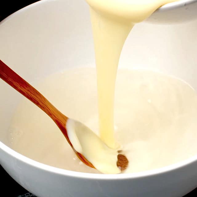 Sweetened condensed milk being poured into gelatin mixture to make rainbow jello.