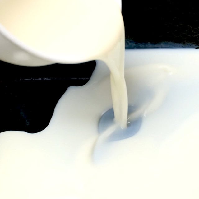 Condensed milk mixture being poured on top of set jello layer.