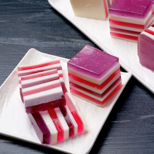 Sliced square rainbow jello on a serving plate.