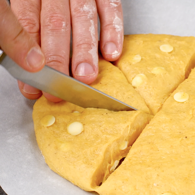 Pumpkin scone dough being cut into wedges.