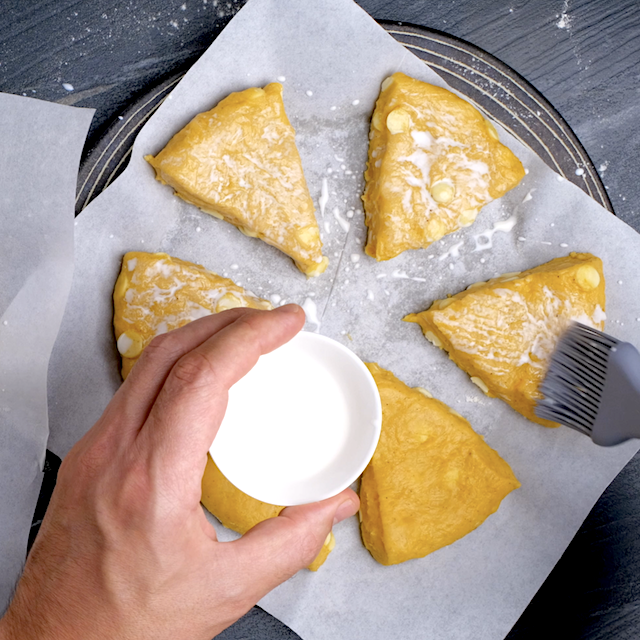Milk being brushed on top of pumpkin scone wedges.