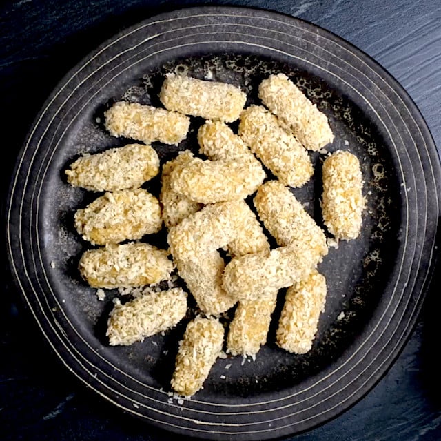 Coated mozzarella sticks on a wax-lined baking sheet.