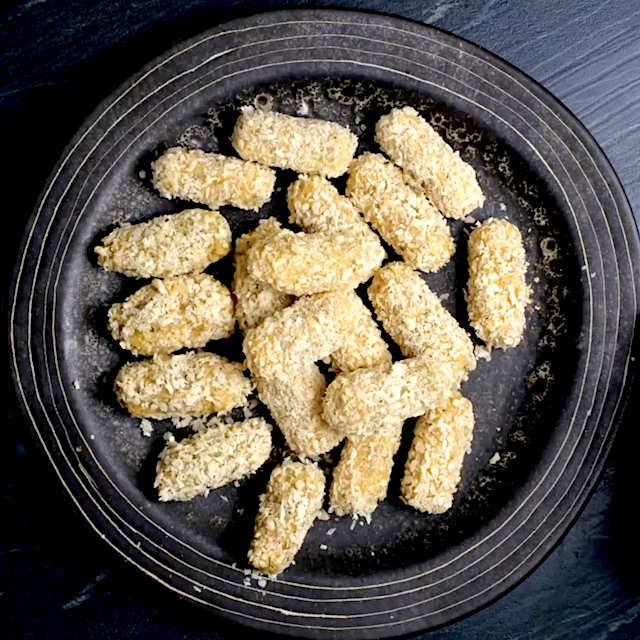 Coated mozzarella sticks on a wax-lined baking sheet.