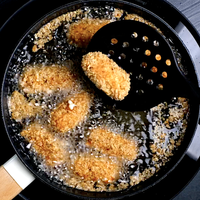 Homemade mozzarella sticks being fried in oil in a saucepan.