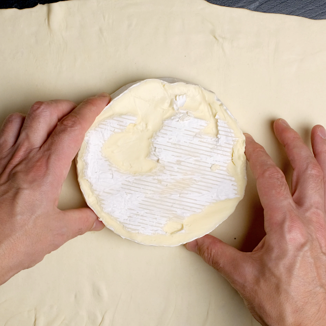 Brie wheel being placed on top of defrosted puff pastry to make brie en croute.