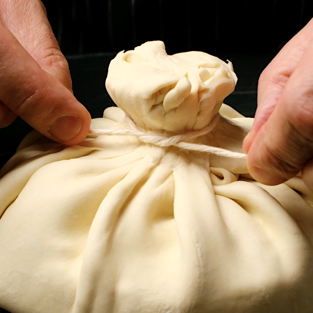 Brie en croute being secured on with kitchen twines.