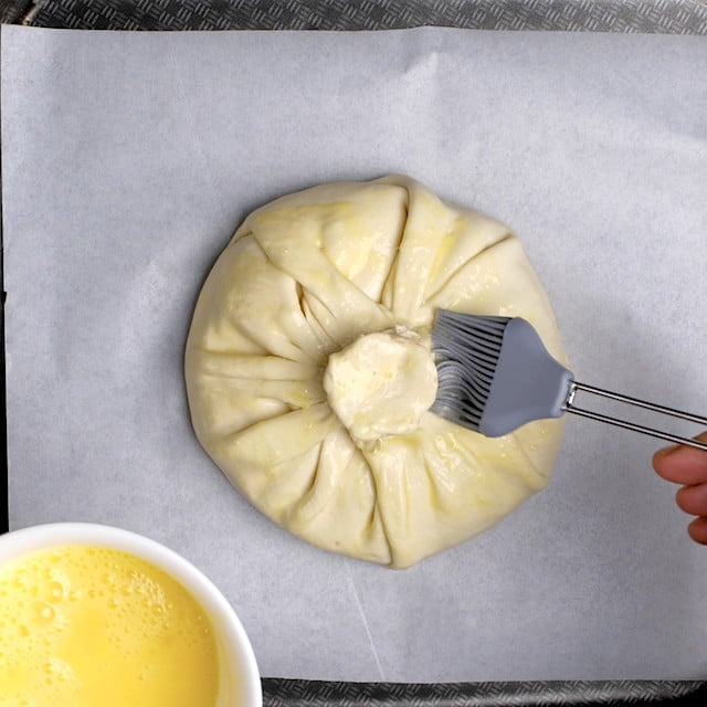 Egg wash being added to brie en croute before baking.