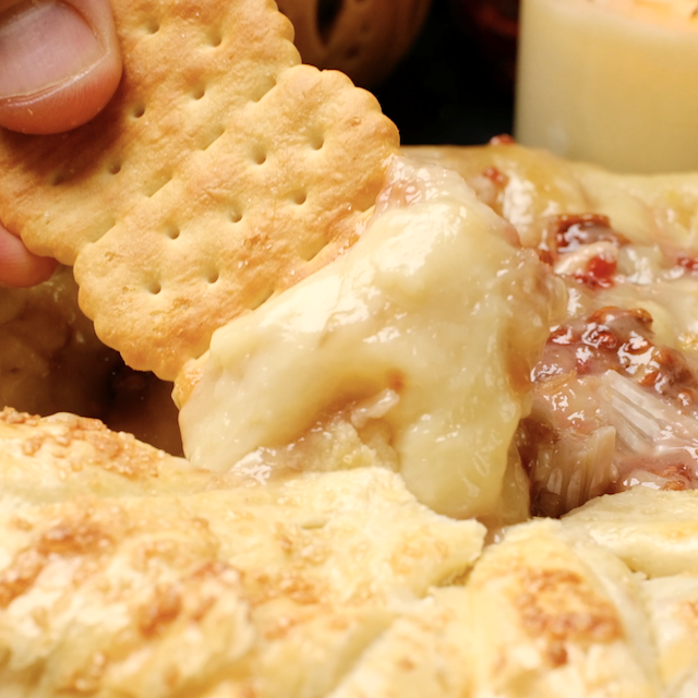 A person dips a cracker into melted brie en croute.