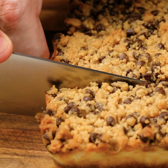 Baked chocolate chip cheesecake being cut into bars.