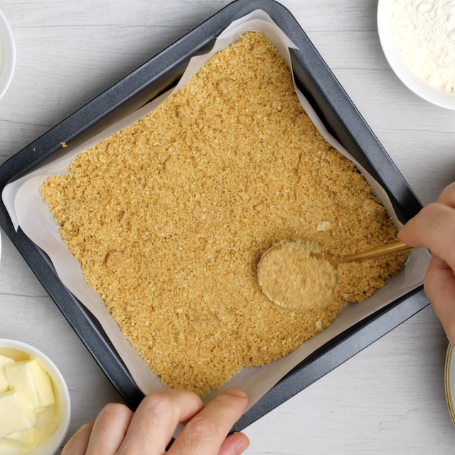 Cheesecake bar based being pressed into lined baking pan.