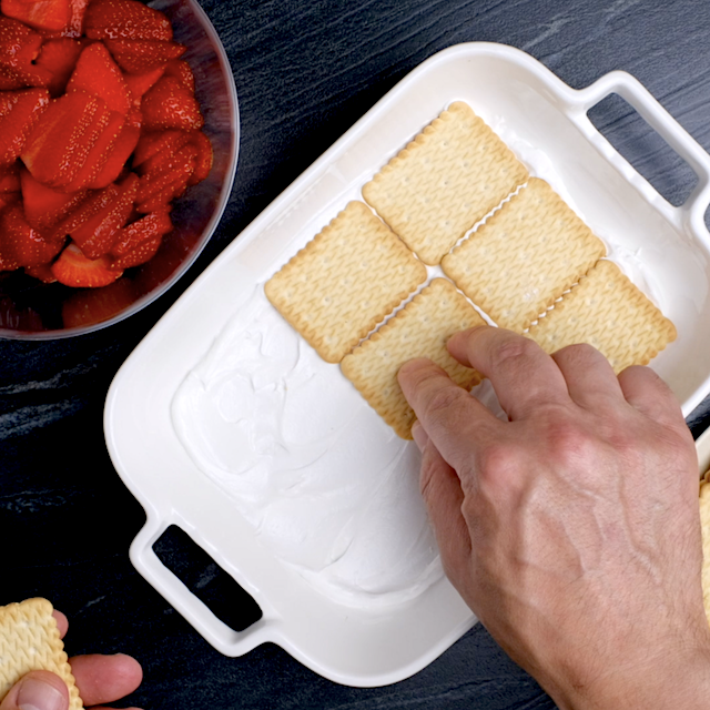 Graham crackers being evenly distributed over cream to make strawberry icebox cake.