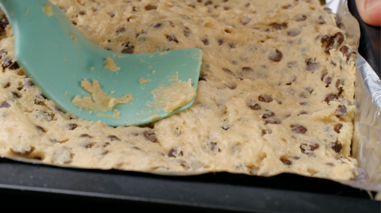 S'mores cookie bar dough being spread evenly in a pan.