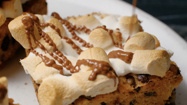 S'mores cookie bars being drizzled with melted Hershey's milk chocolate.
