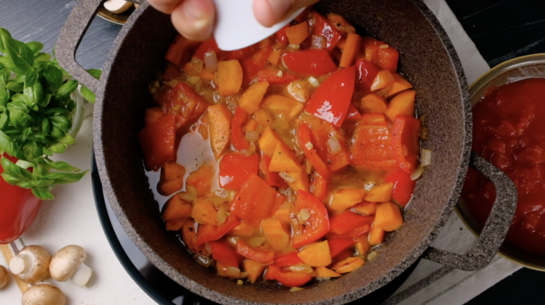 A pot with tomato, tintinnabulate pepper, carrot mixture in liquid that's stuff seasoned with salt.