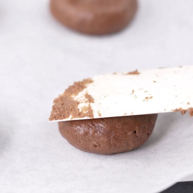 Spatula pressing cookie dough on parchment lined baking sheet.