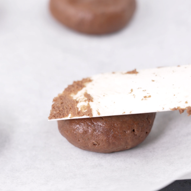 Spatula pressing cookie dough on parchment lined baking sheet.