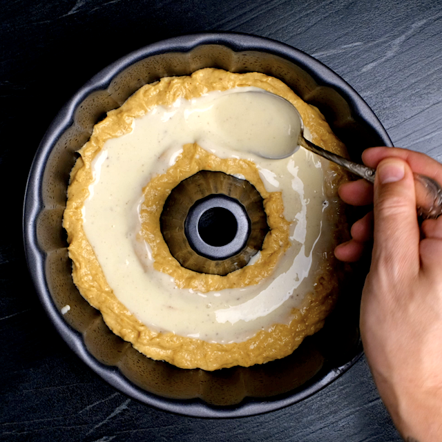 Chilled cream cheese filling being added into a tunnel in pumpkin bundt cake batter inside a bundt pan.