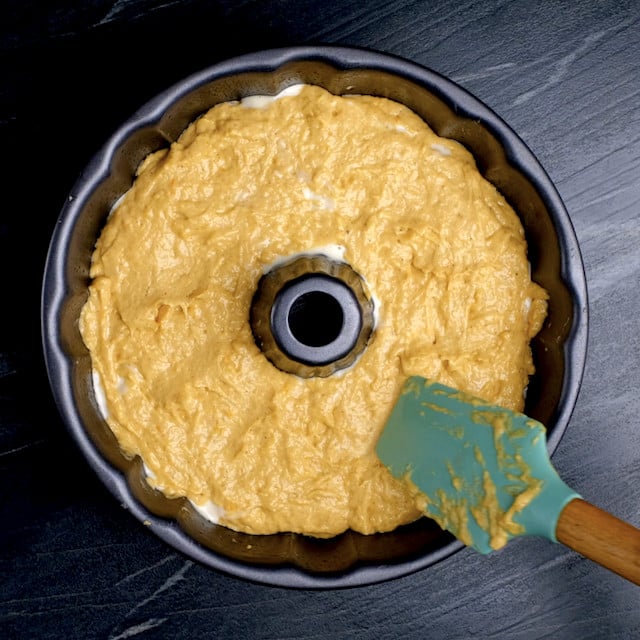 Remaining pumpkin bundt cake batter covering cream cheese filling in a bundt pan.