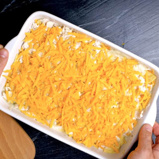 Layered white chicken enchilada casserole being transferred to the fridge overnight before baking.
