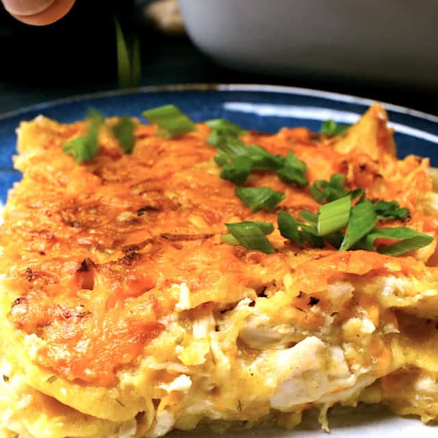 Chopped green onions being garnished on top of freshly baked white chicken enchilada casserole.