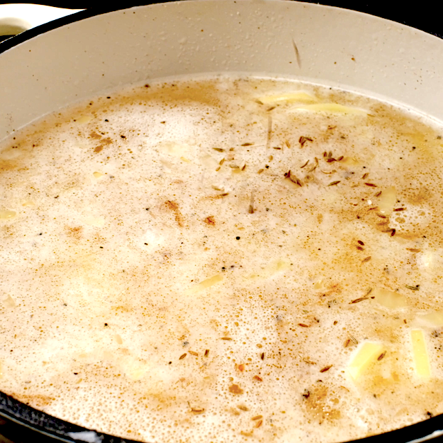Chicken broth with seasonings, potatoes, and sausage being cooked in a pot to make Zuppa Toscana.