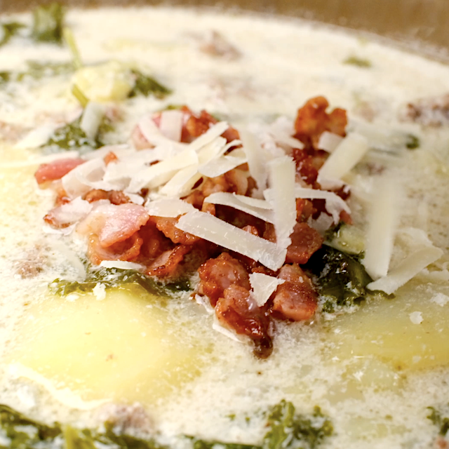 Freshly made zuppa toscana being served with diced bacon and parmesan cheese on top.