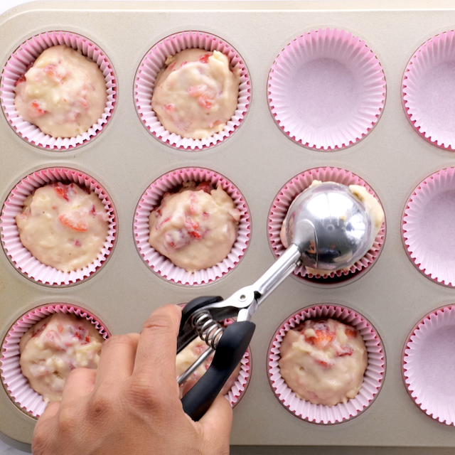 Strawberry cupcake batter being divided into muffin cups.