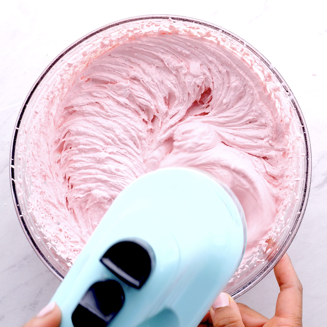 Whipped cream frosting being beaten in a glass bowl for strawberry cupcakes.