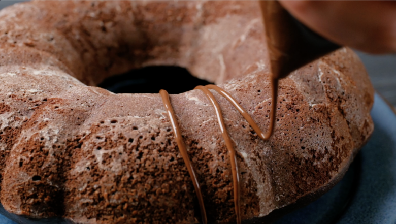 A person is drizzling chocolate on a bundt cake.