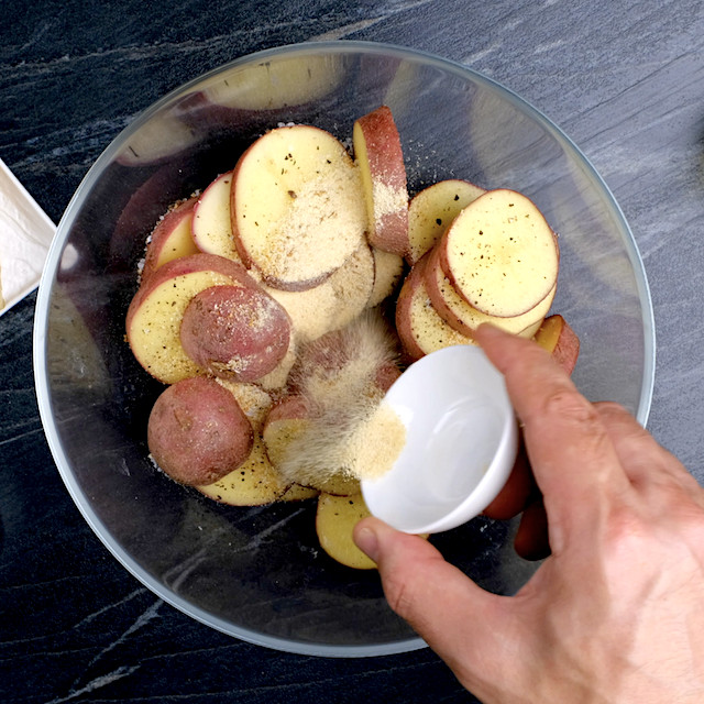 Seasonings being added to a bowl with sliced potatoes to make parmesan roasted potatoes.