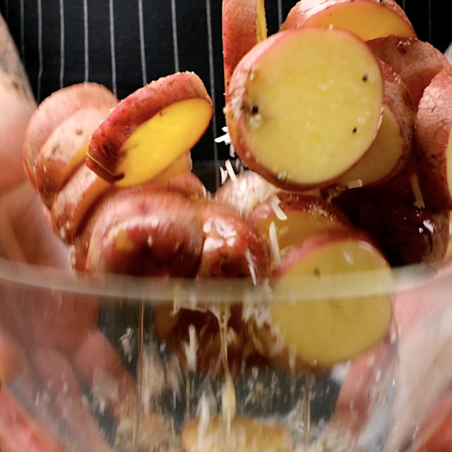 Potatoes being tossed in seasonings and parmesan to make parmesan roasted potatoes.