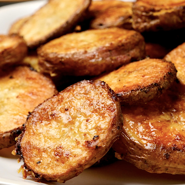 Closeup shot of freshly baked parmesan roasted potatoes on a white plate.