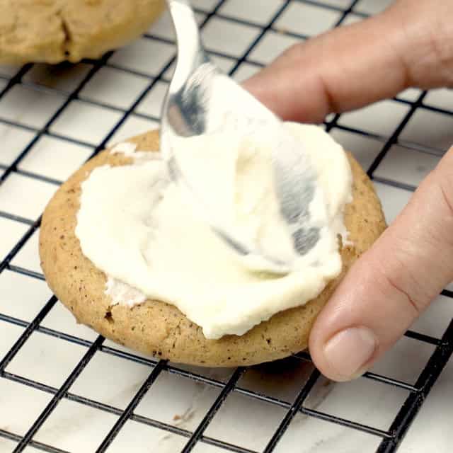 Pumpkin cookies being topped with cream cheese frosting.