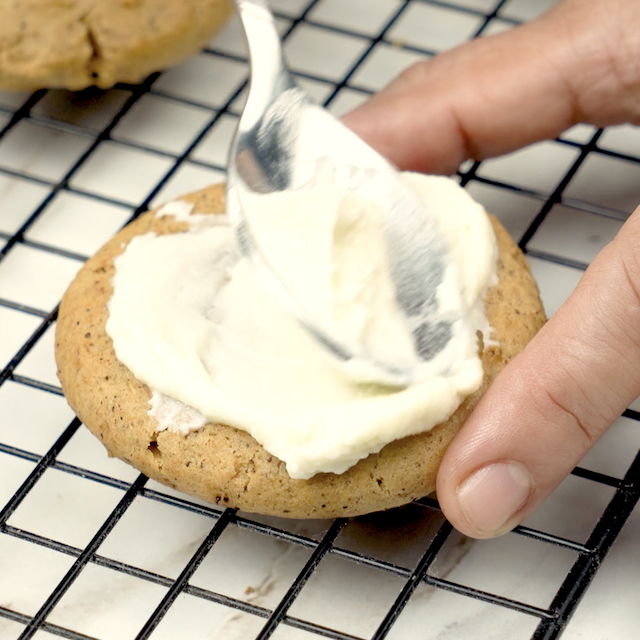 Pumpkin cookies being topped with cream cheese frosting.