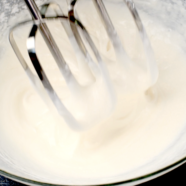 Whipping cream, powdered sugar, and vanilla being whipped in a glass bowl for pumpkin trifle.