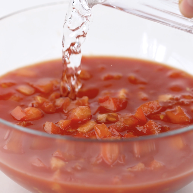 Water being added to diced tomatoes in a bowl.