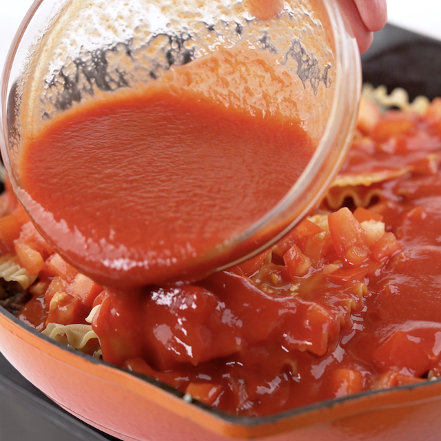Tomato sauce being added to a pan to make skillet lasagna.