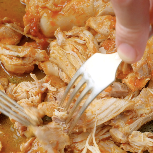 Chicken being shredded with forks to make crockpot salsa chicken.