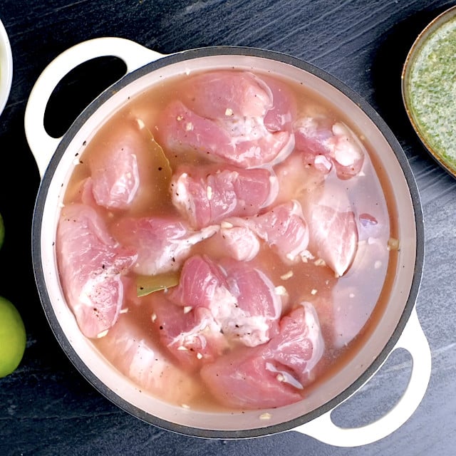 Pork, broth, garlic, and bay leaves in an overproof pot, about to be baked in the oven.