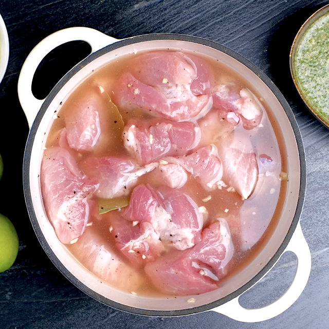 Pork, broth, garlic, and bay leaves in an overproof pot, about to be baked in the oven.