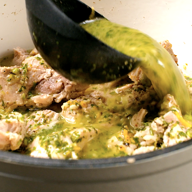 Mojo sauce being poured over pork to allow it to simmer together on the stovetop.
