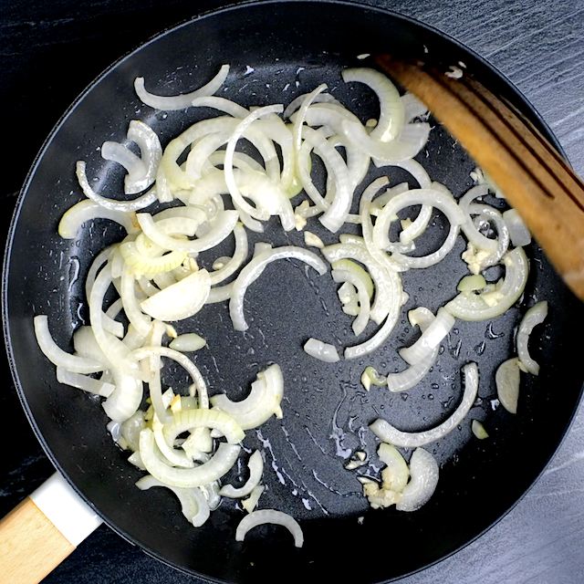Sliced onions and chopped garlic being sautéed in a pan to make Cuban Mojo Pork.