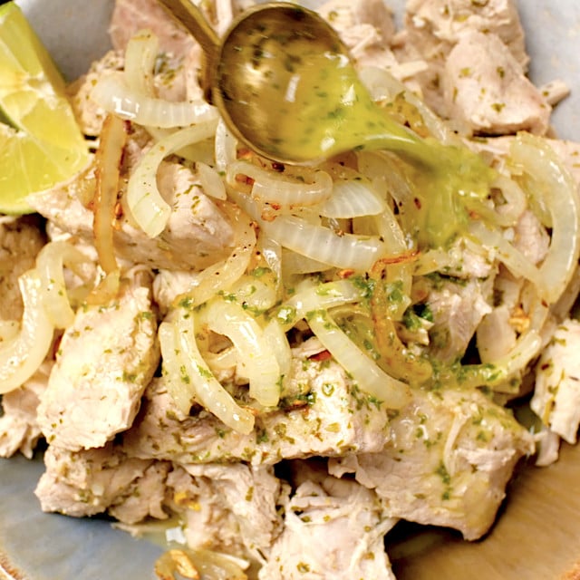 Cuban Pork Mojo being served on a plate with onion mixture on top and a drizzle of Mojo sauce.