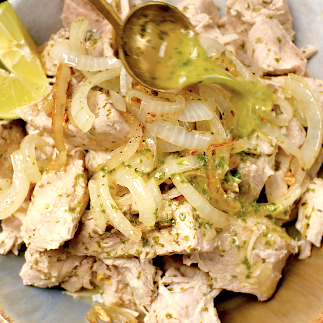 Cuban Pork Mojo being served on a plate with onion mixture on top and a drizzle of Mojo sauce.