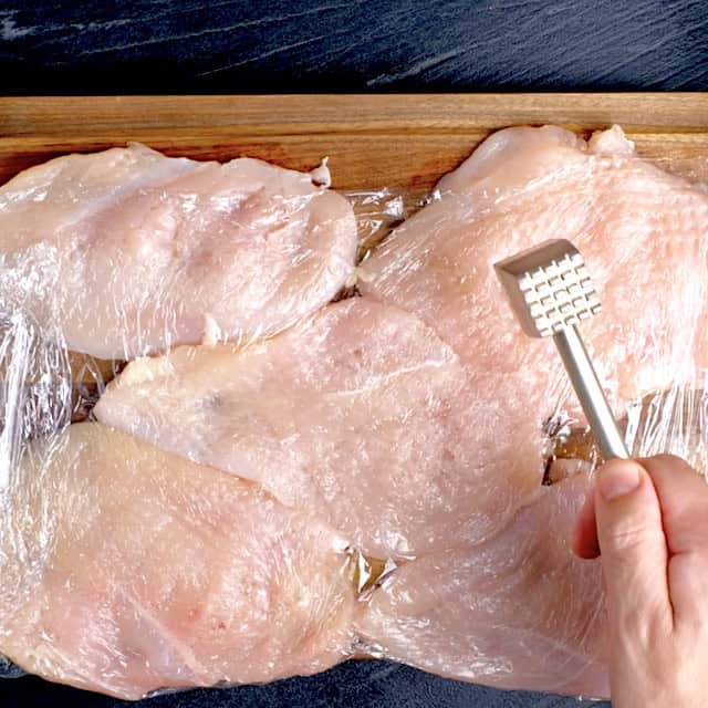Boneless, skinless chicken breast being pounded to an even thickness to make parmesan crusted chicken.