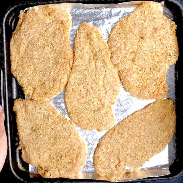 Breadcrumb coated chicken on a baking pan, ready to be baked to make parmesan crusted chicken.